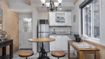 A modern kitchen with white cabinets, a stainless steel refrigerator, a microwave, and a wooden dining table with stools.