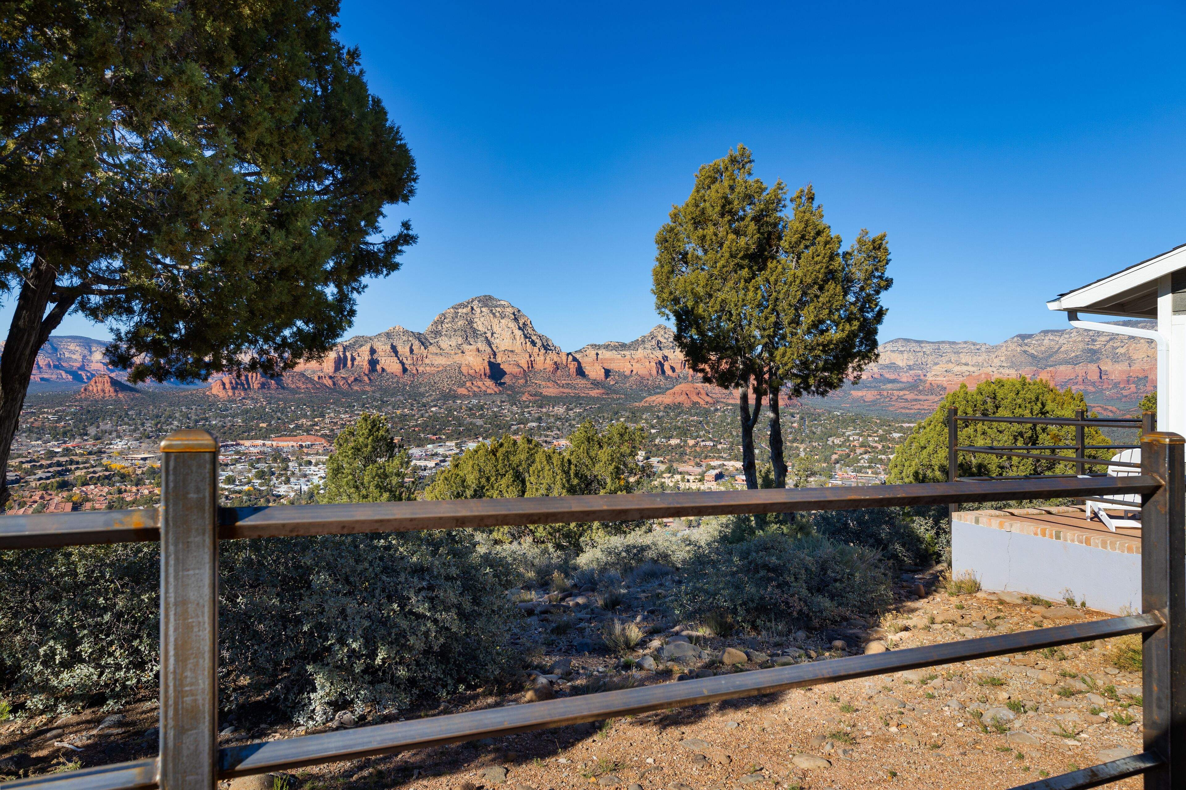 A view from a balcony with a metal railing, overlooking a valley with red rock formations and a town below.