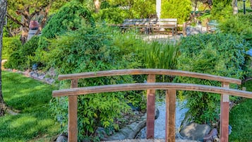 A wooden bridge over a pond with a bench and lush greenery in the background.