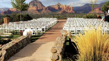 Un salón de bodas al aire libre con hileras de sillas blancas, un sendero de piedra y montañas al fondo.