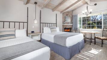 A bedroom with two beds, a fireplace, a dining table, and a view of the outdoors.