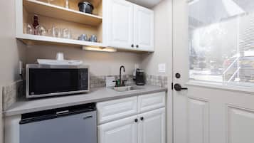 A compact kitchen with white cabinets, a microwave, a coffee maker, and a dishwasher.