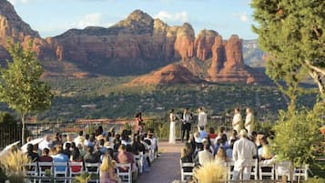 An outdoor wedding ceremony with guests seated in rows facing a couple at the altar, set against a backdrop of red rock formations.