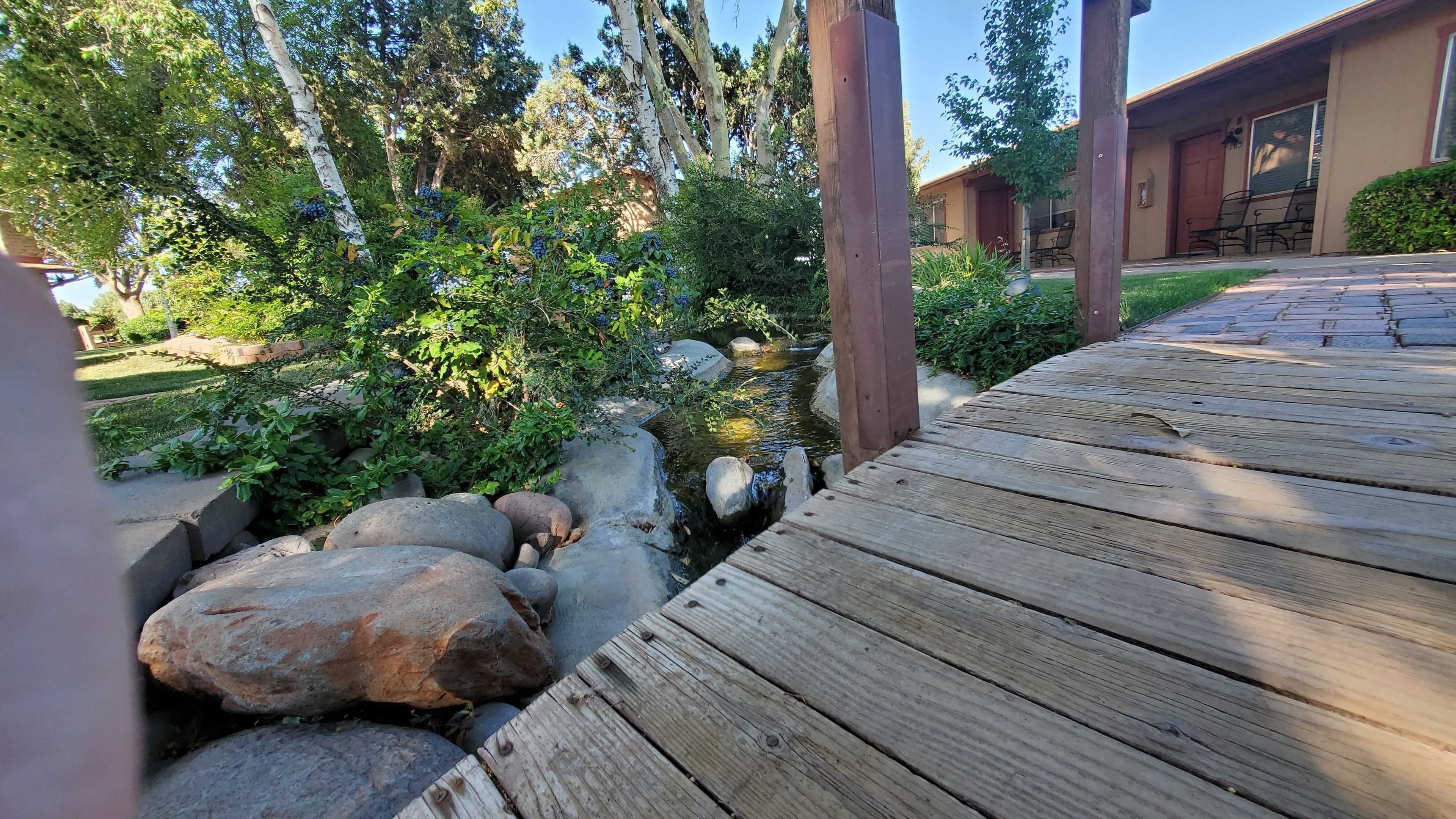 A wooden deck leading to a small stream with rocks and greenery.