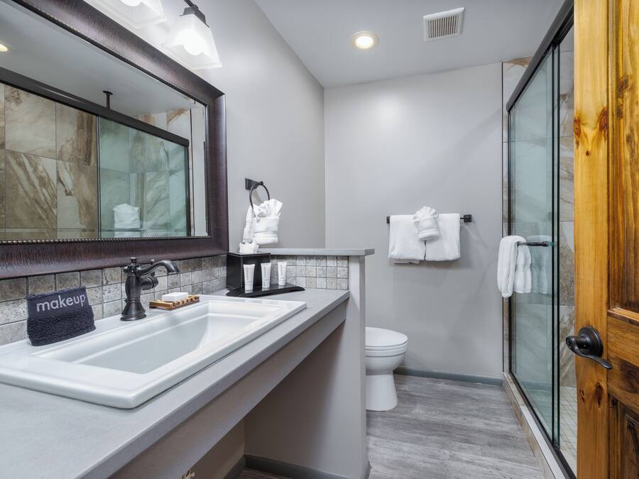 A modern bathroom with a large mirror, a sink, a toilet, and a glass shower enclosure.
