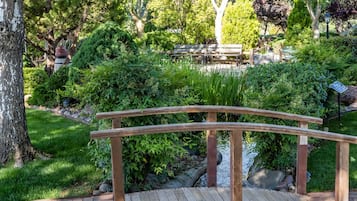 A wooden bridge over a small stream in a garden with a bench and a sign.