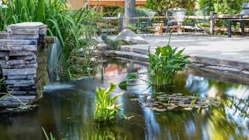 Ein friedlicher Garten mit einem Teich, einem Steine Wasserfall, üppiger Bepflanzung und einer hölzernen Bank.