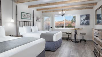 A bedroom with two beds, a desk, and a dresser. There is a window with a view of red rock formations.