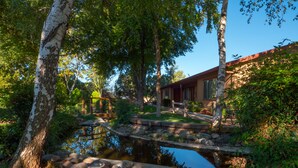 Un jardí tranquil amb un estany, un pont de fusta i una casa amb teulada vermella.