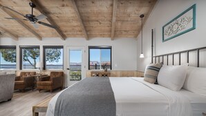 A bedroom with a large bed, a ceiling fan, a desk, and a view of the mountains.