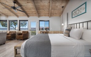 A bedroom with a large bed, a ceiling fan, a desk, and a view of the mountains.