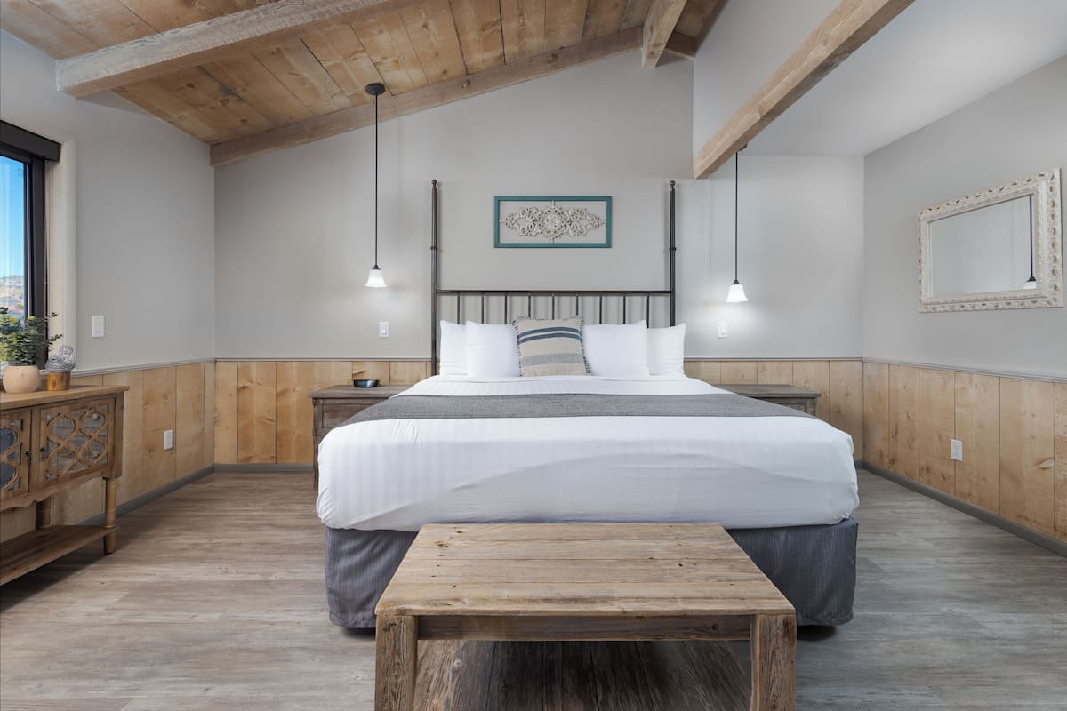 Quarto com cama grande, cabeceira de madeira, mesas de cabeceira, um banco de madeira e teto de madeira.