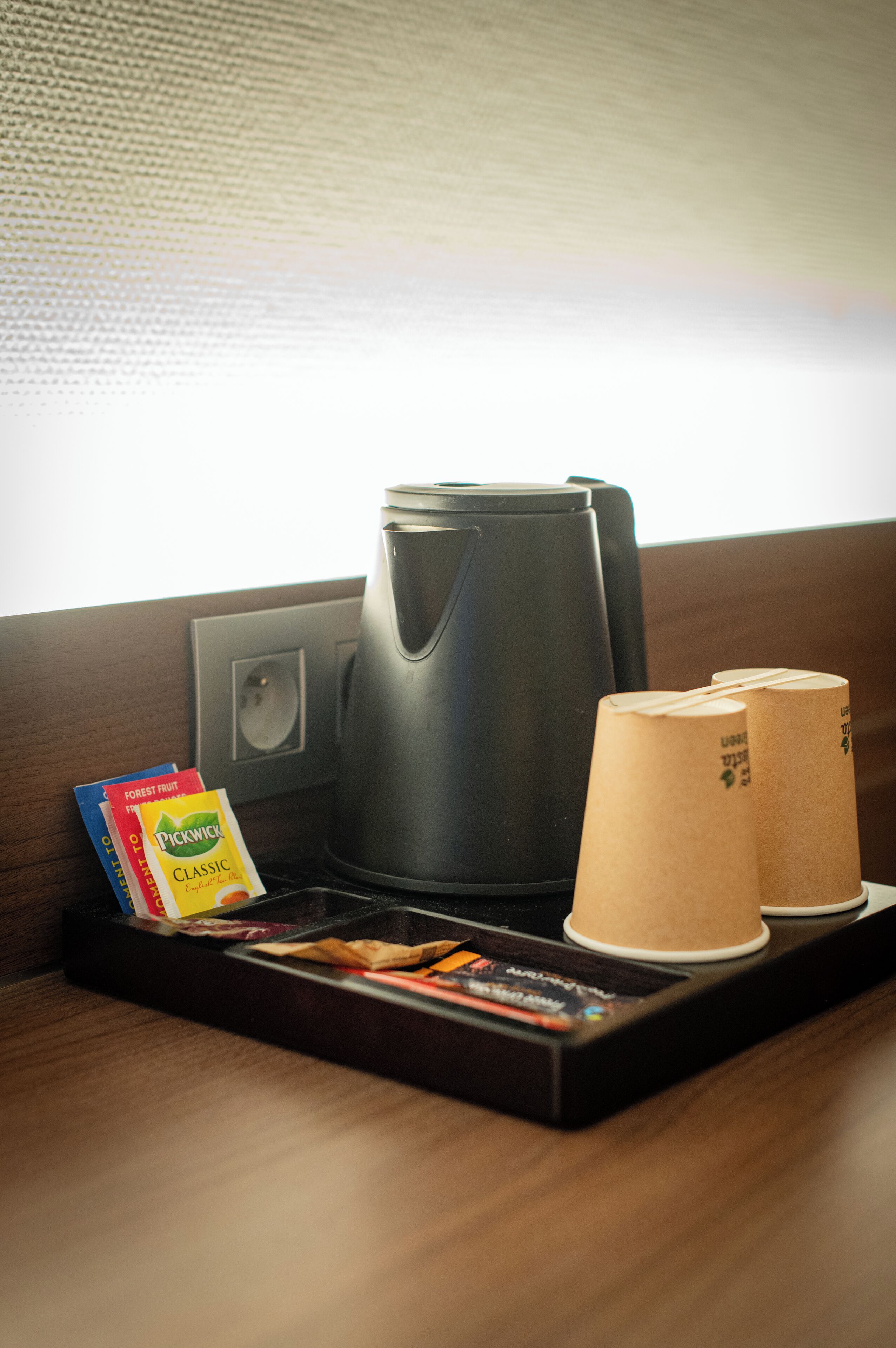 A coffee maker, two paper cups, and a tray with books on a wooden surface.