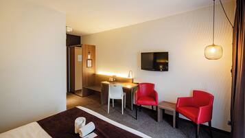 Habitación de hotel con cama, escritorio, dos sillas rojas, televisor y lámpara colgante.