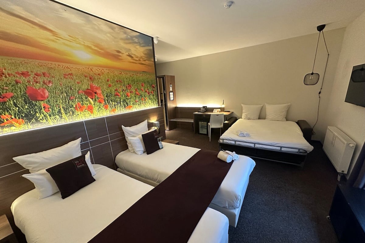 Une chambre d’hôtel avec deux lits, un bureau, une chaise, une grande fresque murale à motifs floraux et un téléviseur.