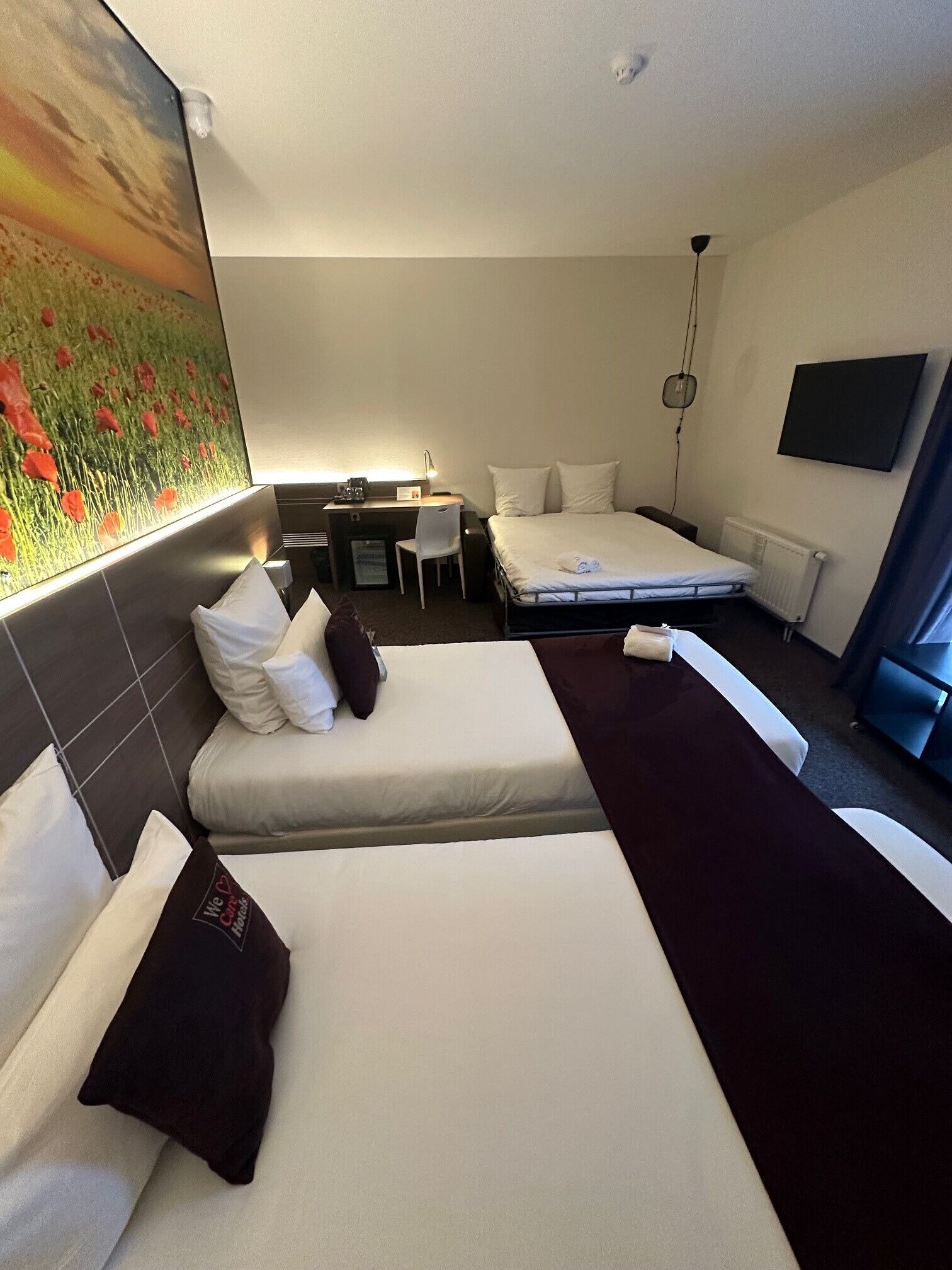 A hotel room with two beds, a desk, a chair, a TV, and a painting on the wall.