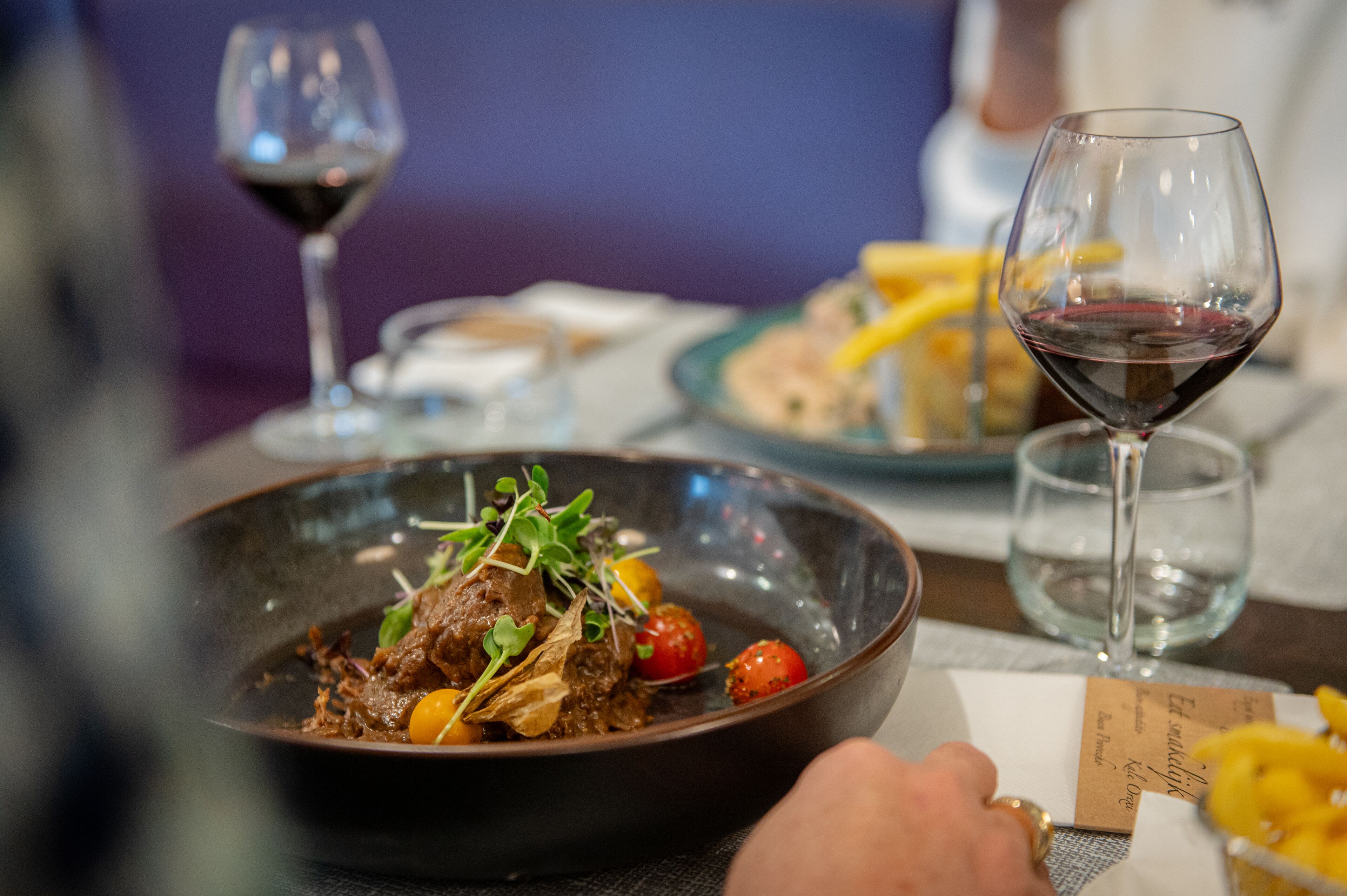 A dining table with a bowl of food, a wine glass, and a menu.