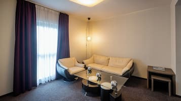 A modern hotel room with a sofa, a glass coffee table, and a small side table.
