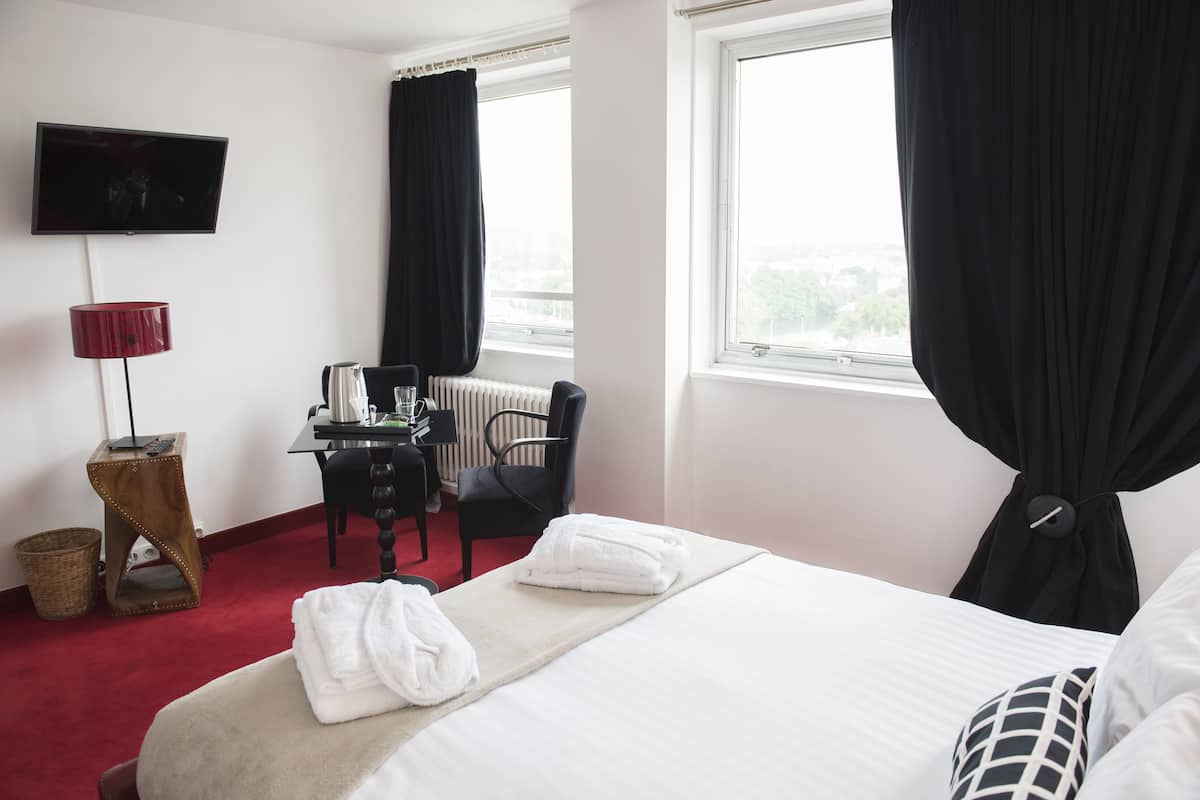 Une chambre d’hôtel équipée d’un lit, d’un bureau, d’une chaise, d’une télévision et d’une fenêtre avec des rideaux.