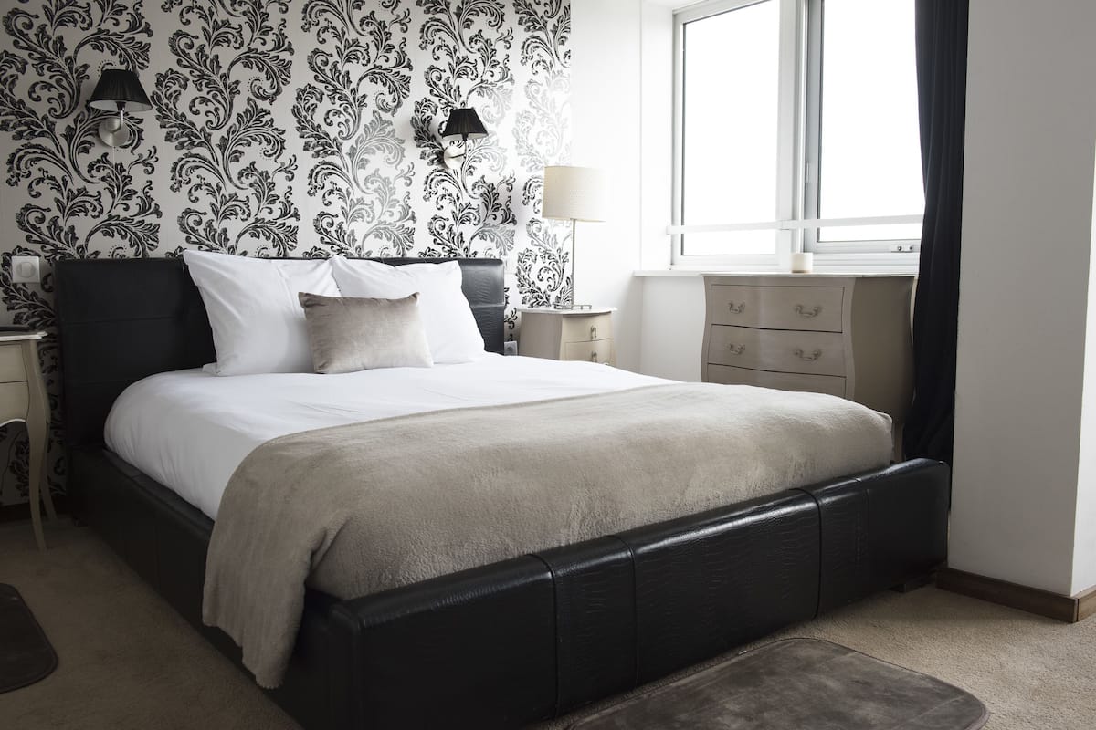 Une chambre à coucher bien rangée, avec un grand lit, deux lampes de chevet, une commode et une fenêtre avec des rideaux.