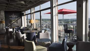 A modern indoor space with multiple seating areas, large windows offering a view of a cityscape, and a red umbrella.