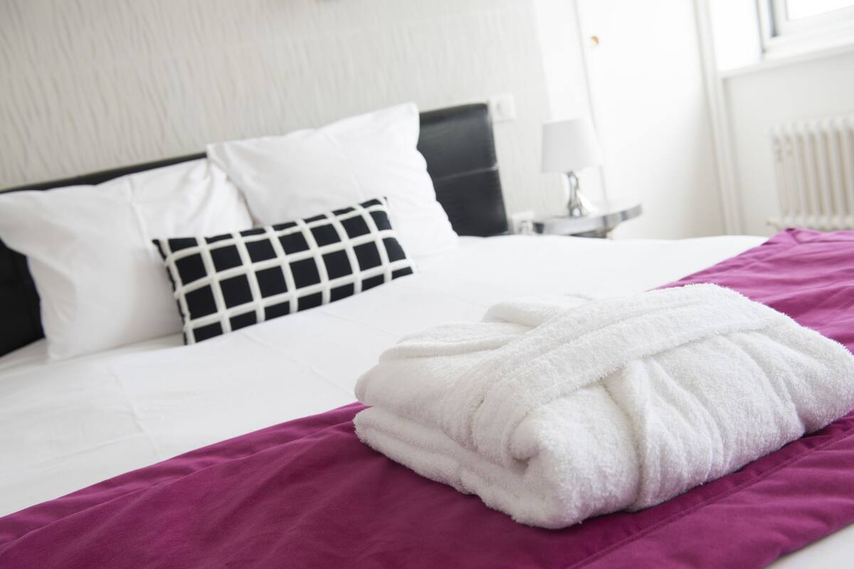 Un lit bien fait, avec du linge de lit blanc et un plaid violet.
