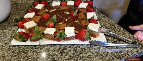 A dessert tray with brownies and strawberries on a granite countertop.