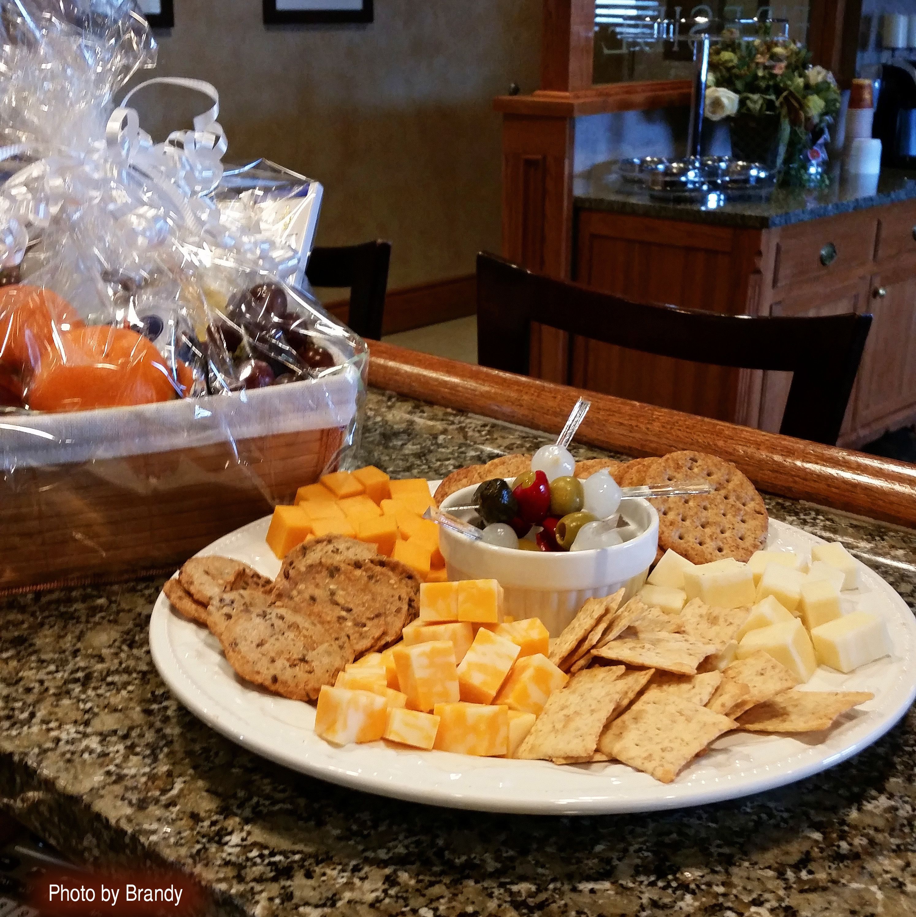 A plate with cheese, crackers, and a bowl of olives and grapes.