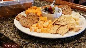 A plate with cheese, crackers, and a bowl of olives and grapes.