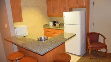 Una cocina con encimeras de granito, armarios de madera, un refrigerador blanco y una silla de madera.