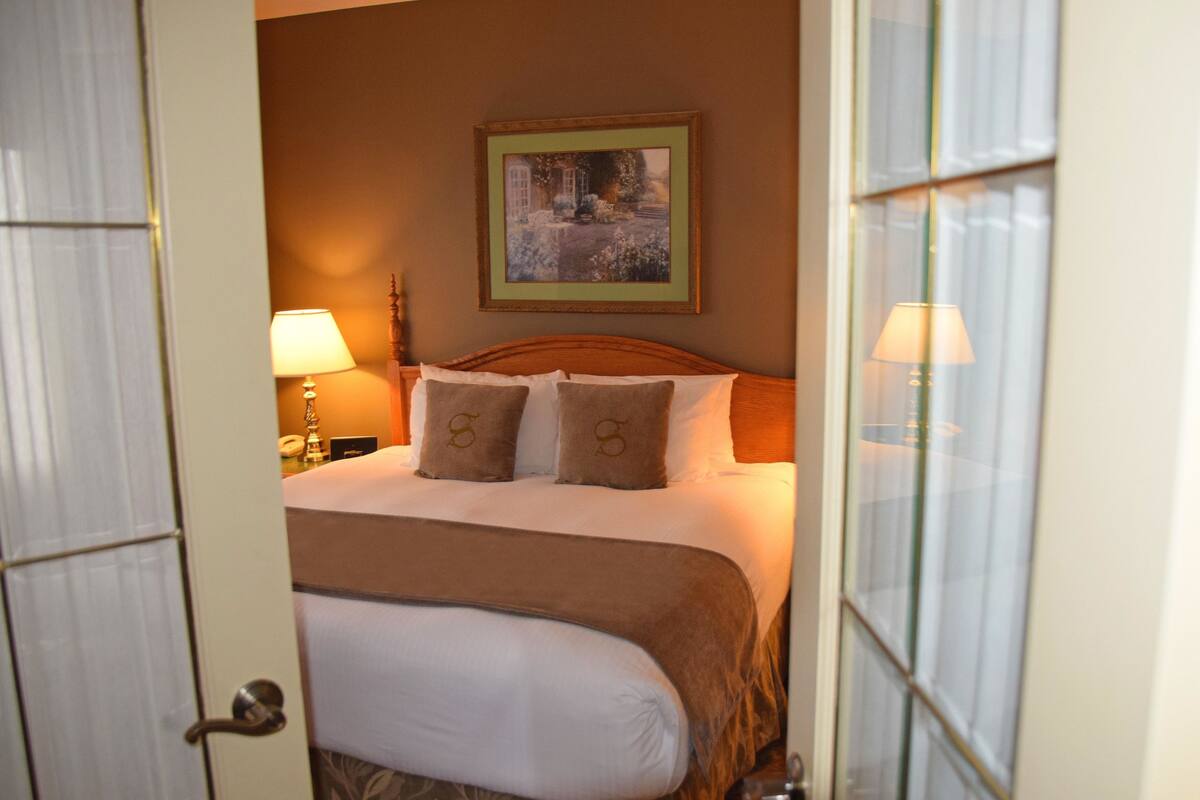 A hotel room with a bed, two bedside lamps, a framed picture on the wall, and a door with a glass panel.