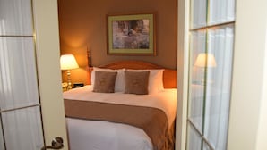 A hotel room with a bed, two bedside lamps, a framed picture on the wall, and a door with a glass panel.