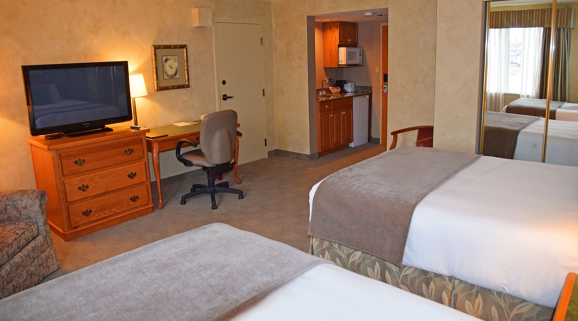 Une chambre d’hôtel avec deux lits, un bureau avec une chaise, une télévision, un four à micro-ondes et une petite kitchenette.