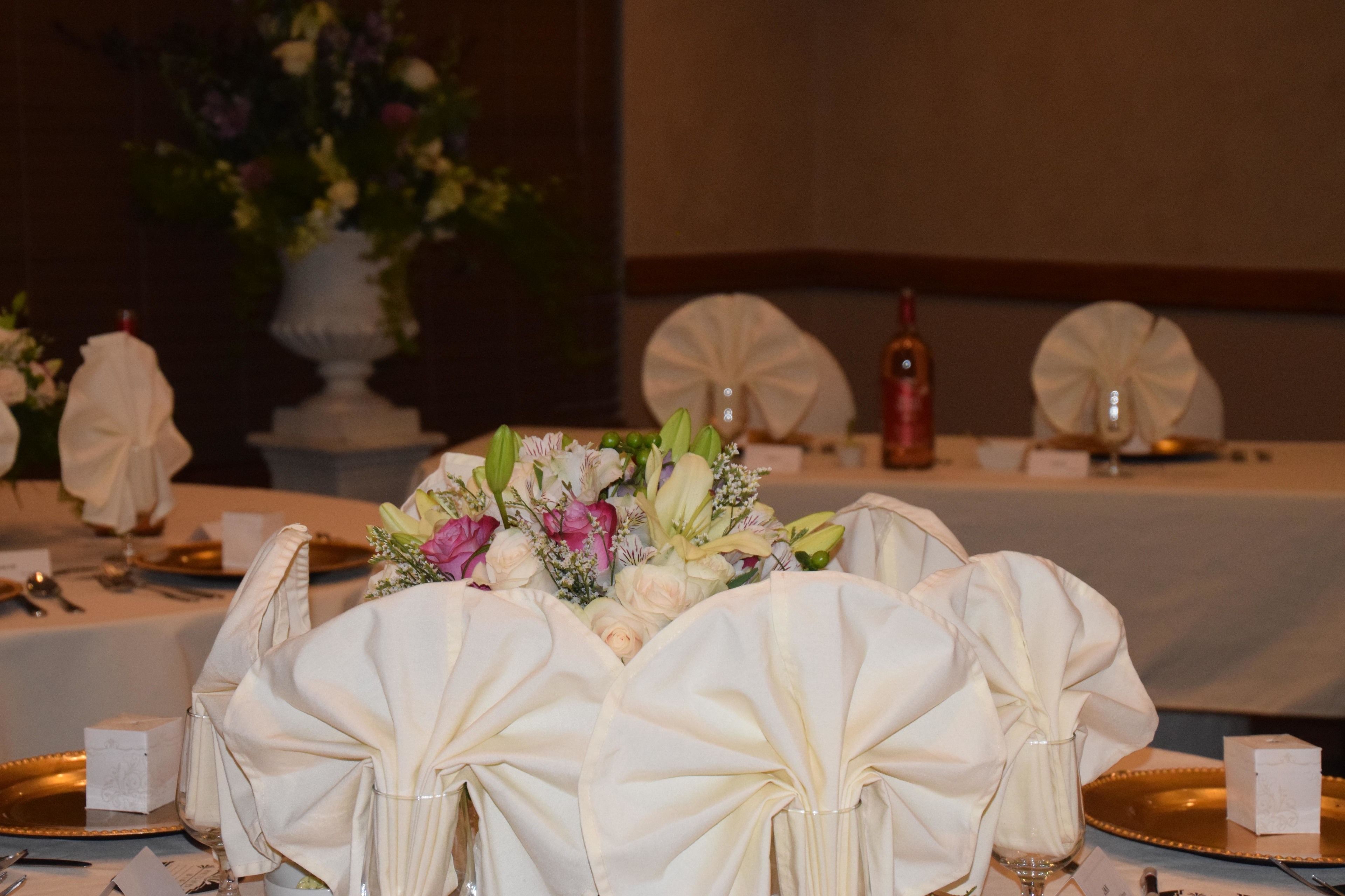 A table set for a formal event with white tablecloths, gold chargers, and a centerpiece of flowers.