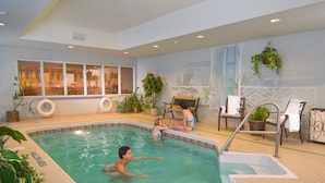 An indoor swimming pool with clear water, surrounded by potted plants and sunlit windows.