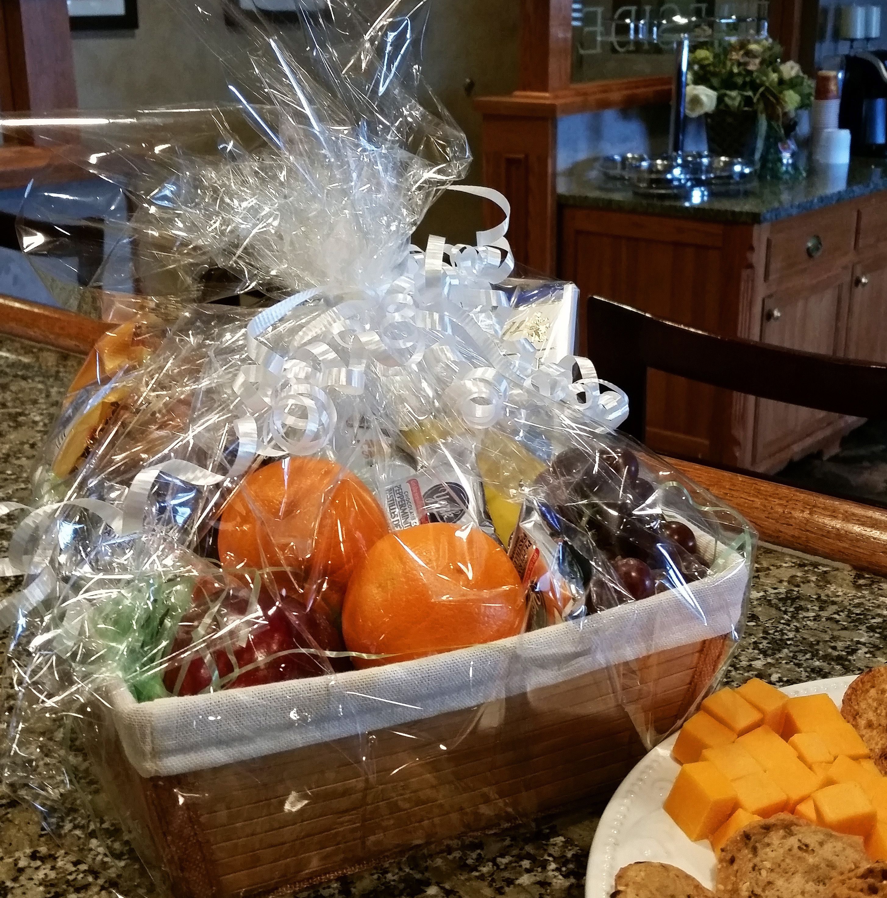 A gift basket with various fruits and vegetables wrapped in clear plastic and tied with ribbons, placed on a kitchen counter.