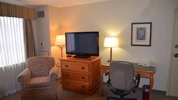 Een hotelkamer met een houten bureau, een televisie, een stoel, een lamp en een schilderij aan de muur.