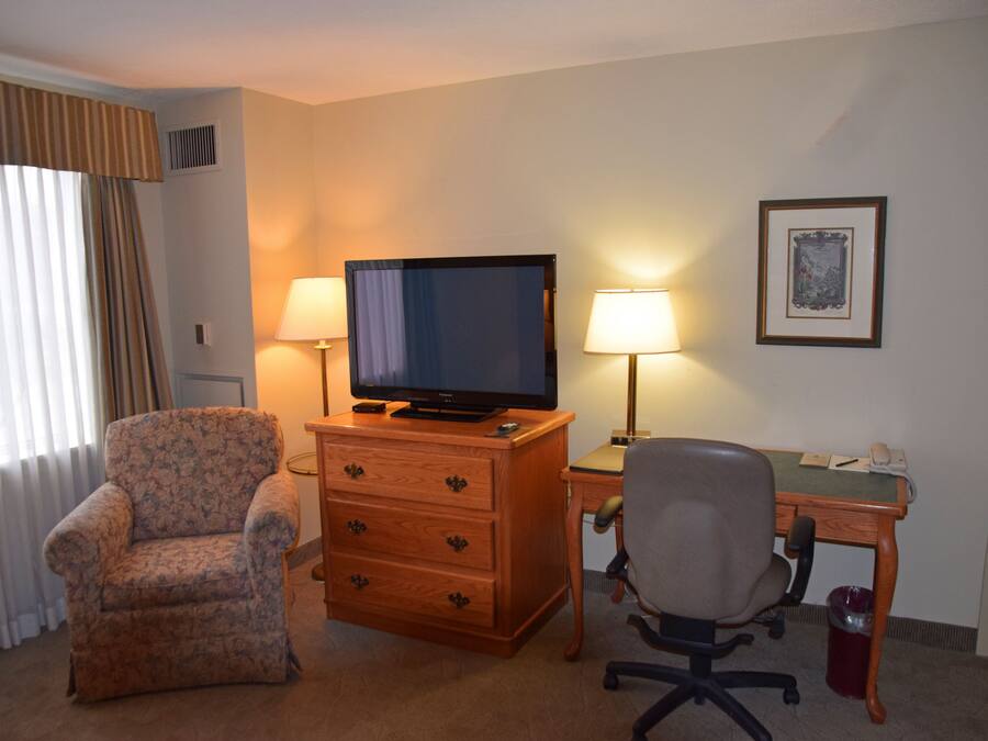Habitación de hotel con un escritorio de madera, televisión, silla, lámpara y un cuadro en la pared.