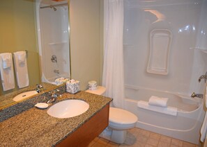 A bathroom with a granite countertop, a sink, a toilet, and a bathtub.