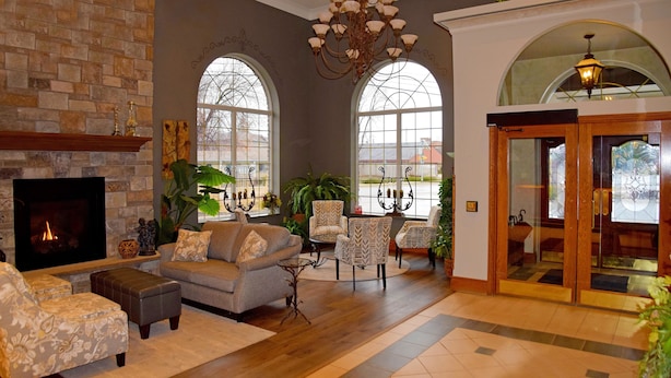 A spacious living room with a fireplace, comfortable seating, large windows, and a chandelier.