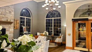 A cozy living room with a fireplace, two large arched windows, and a chandelier.