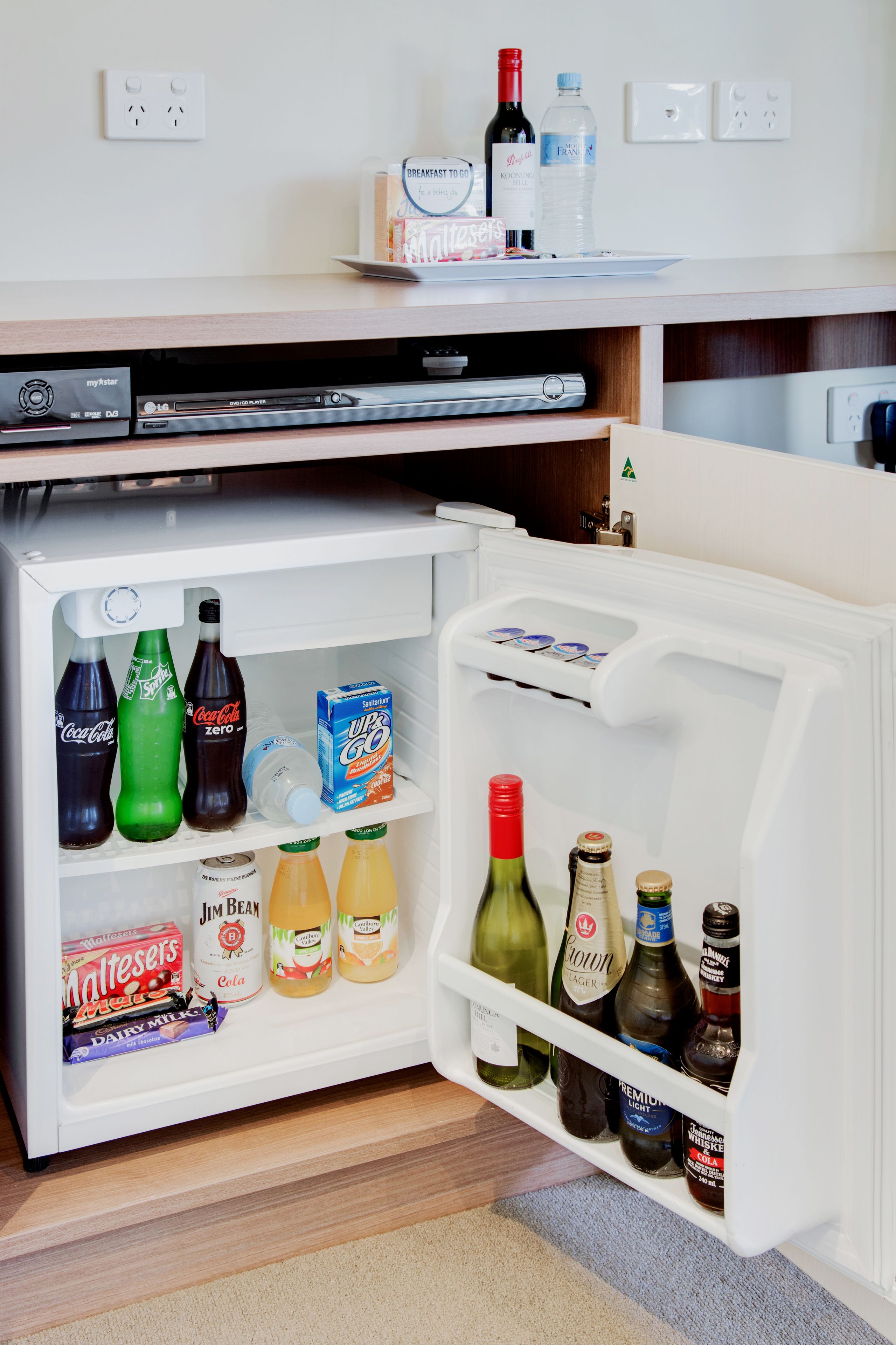 Un petit réfrigérateur rempli de boissons et d’en-cas, un four à micro-ondes et une petite étagère avec des produits pour le petit-déjeuner.