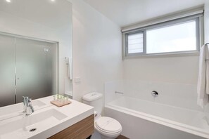 A modern bathroom with a large mirror, a white sink, a toilet, and a bathtub.
