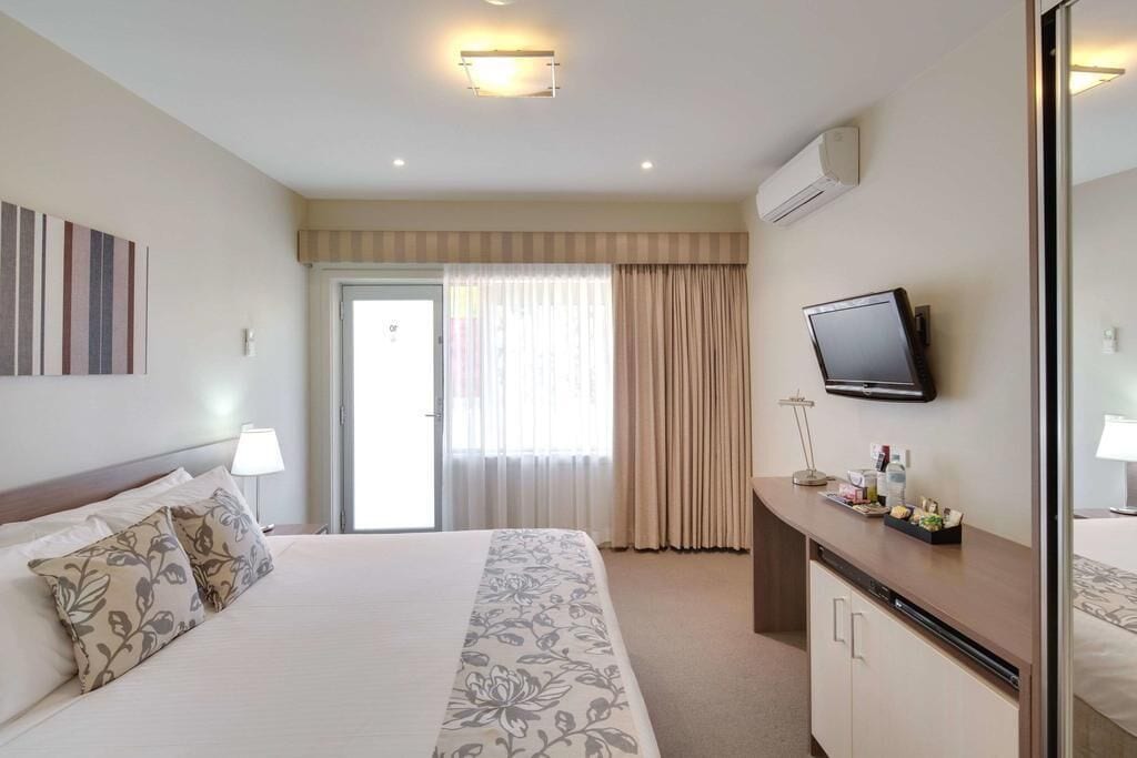 A hotel room with a bed, a desk, a television, and a sliding door to the balcony.