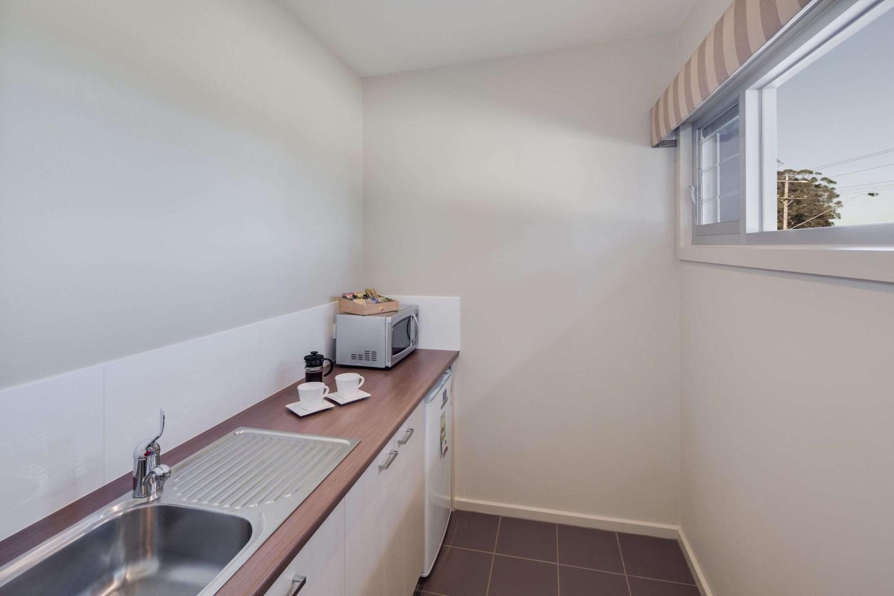 A compact kitchen with a sink, microwave, and a small countertop with a toaster and cups.