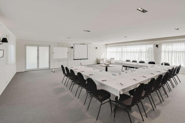 A conference room with a long table, chairs, a projector screen, and a whiteboard.