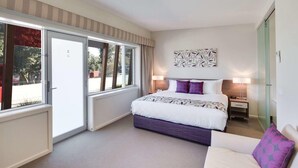 A hotel room with a bed, a nightstand, a lamp, a window, and a door. - Drouin Motel (Drouin)
