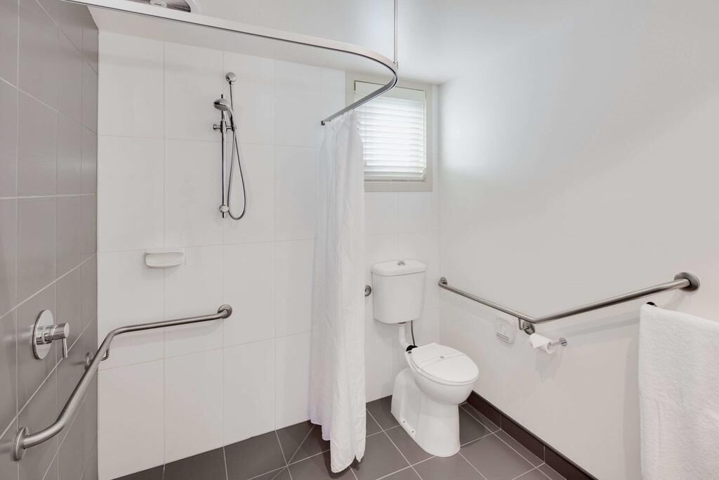 A modern bathroom with a shower, toilet, and handrails.