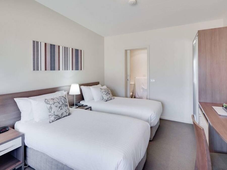 Quarto de hotel com duas camas, uma mesa e porta de banheiro.