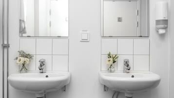 A modern bathroom with two white sinks, mirrors, and a white trash bin.